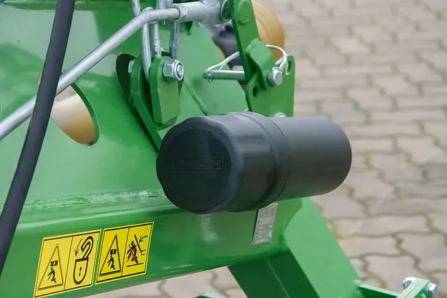 Nærbilde av drivakselbeskyttelse og sikkerhetsklistremerker på grønn landbruksmaskin.