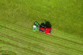 Luftfoto av traktor med slåmaskin som lager parallelle rekker i gresset.
