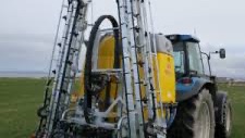 Rød traktor med slåmaskin står på en eng med nyslått gress en solrik dag.