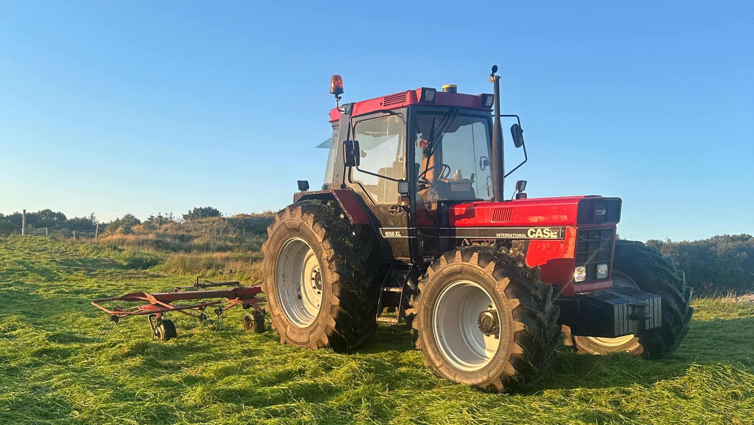 Rød traktor med slåmaskin står på en eng med nyslått gress en solrik dag.