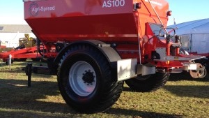 Rød traktor med slåmaskin står på en eng med nyslått gress en solrik dag.