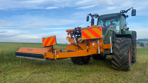 Rød traktor med slåmaskin står på en eng med nyslått gress en solrik dag.