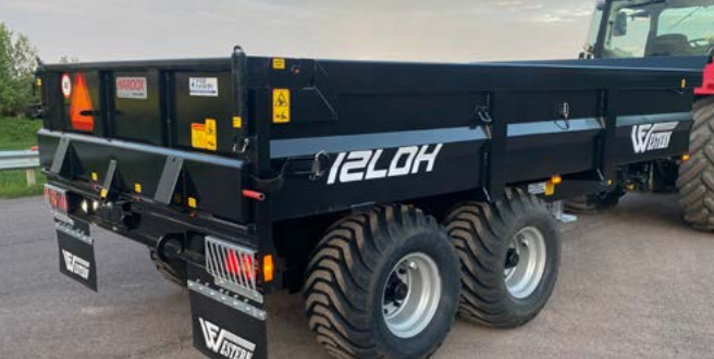 Rød traktor med slåmaskin står på en eng med nyslått gress en solrik dag.