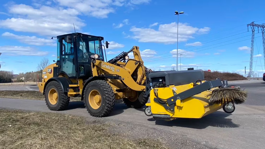 Grønn traktor med stor oransje V-plog rydder snø foran seg.