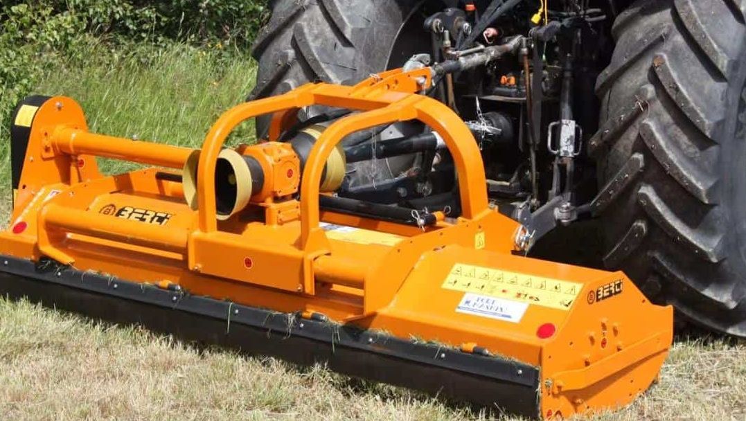 Oransje beitepusser montert på traktor klargjort for arbeid.