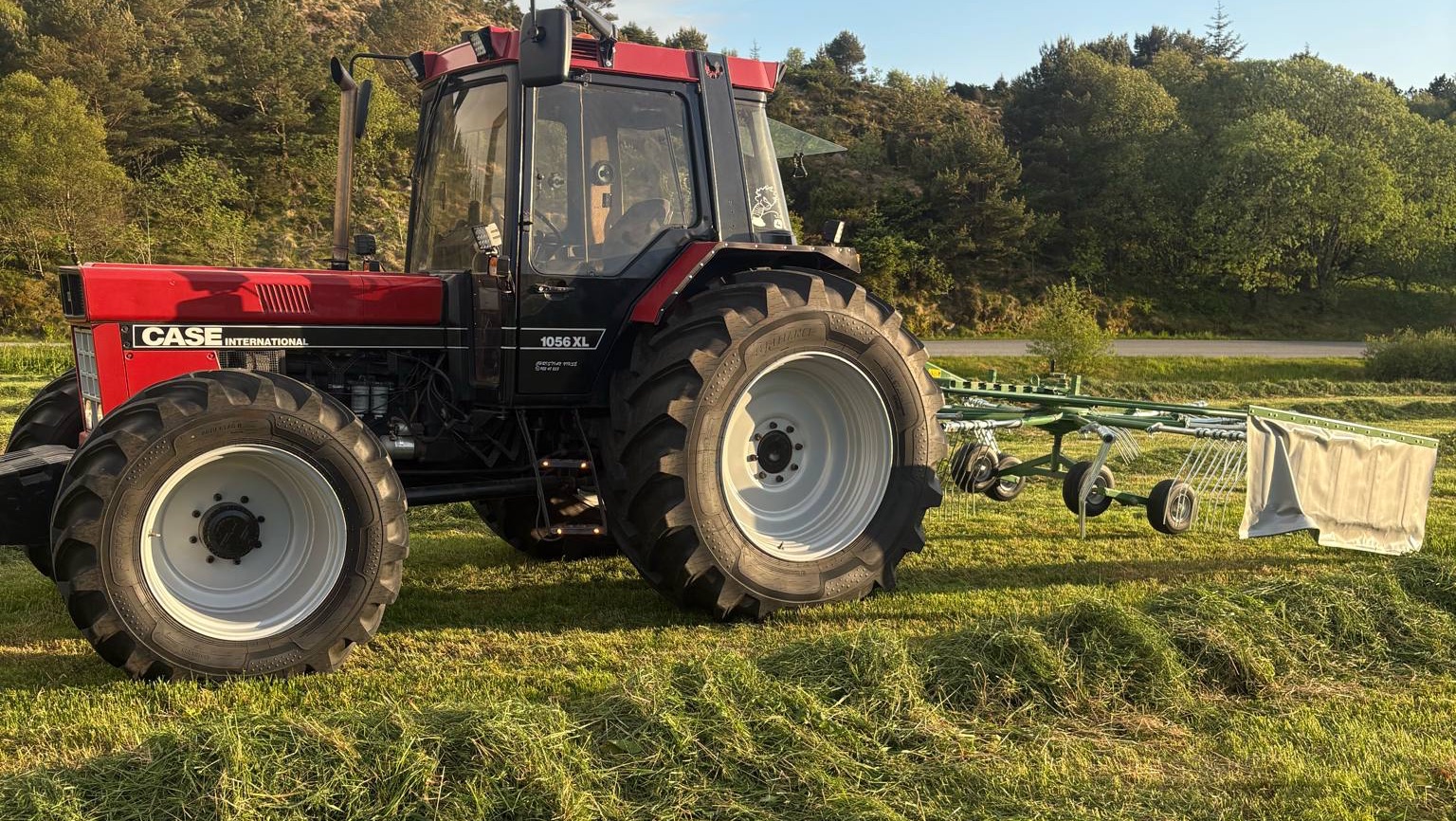 En grønn traktor med rundballepakker som pakker høyballer i plast ute på et jorde.