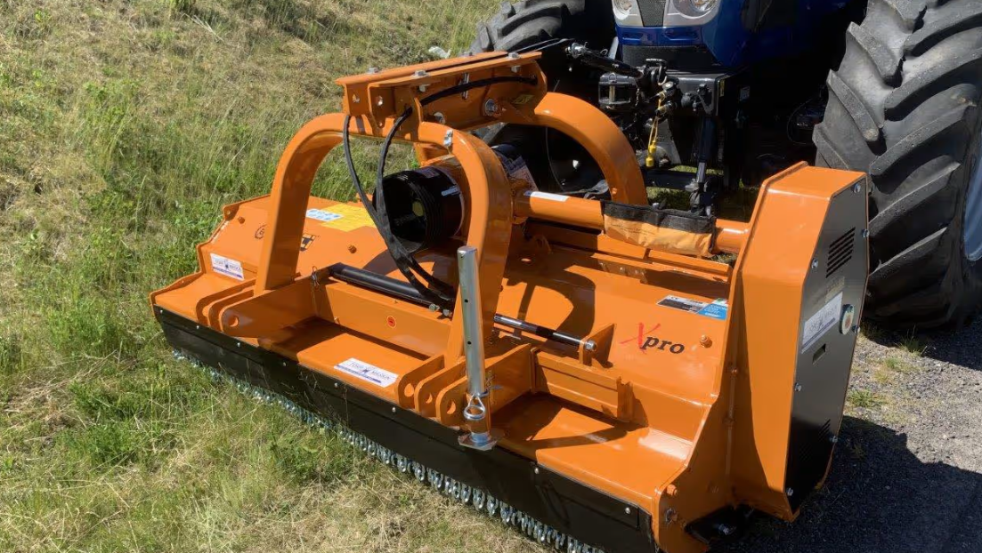 Rød traktor med slåmaskin står på en eng med nyslått gress en solrik dag.