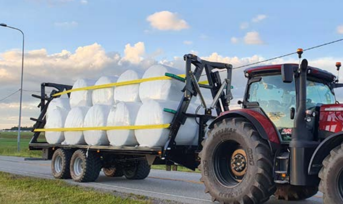 Rød traktor med slåmaskin står på en eng med nyslått gress en solrik dag.