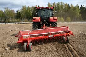 Rød traktor med slåmaskin står på en eng med nyslått gress en solrik dag.