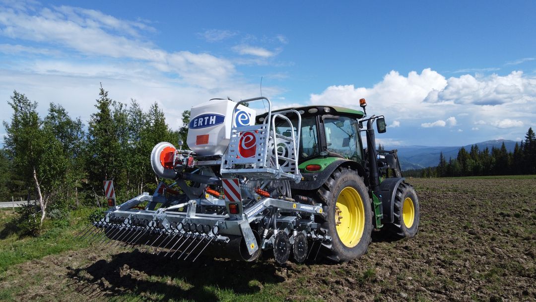 Rød traktor med slåmaskin står på en eng med nyslått gress en solrik dag.