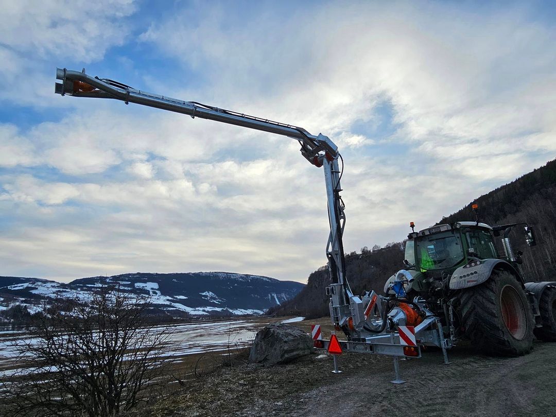 Rød traktor med slåmaskin står på en eng med nyslått gress en solrik dag.