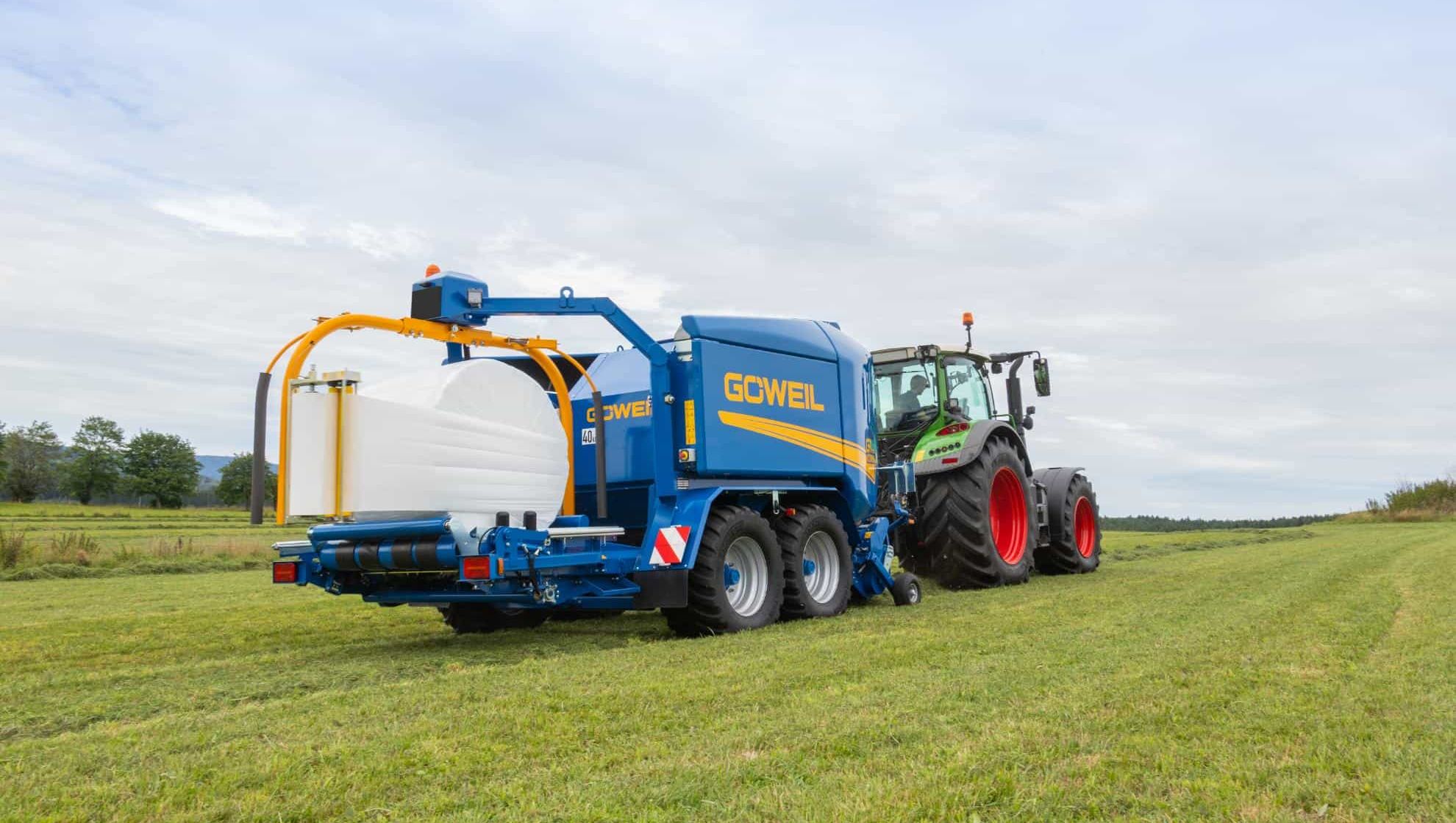 Traktor trekker blå Goweil rundballepresse og pakker på jordet.