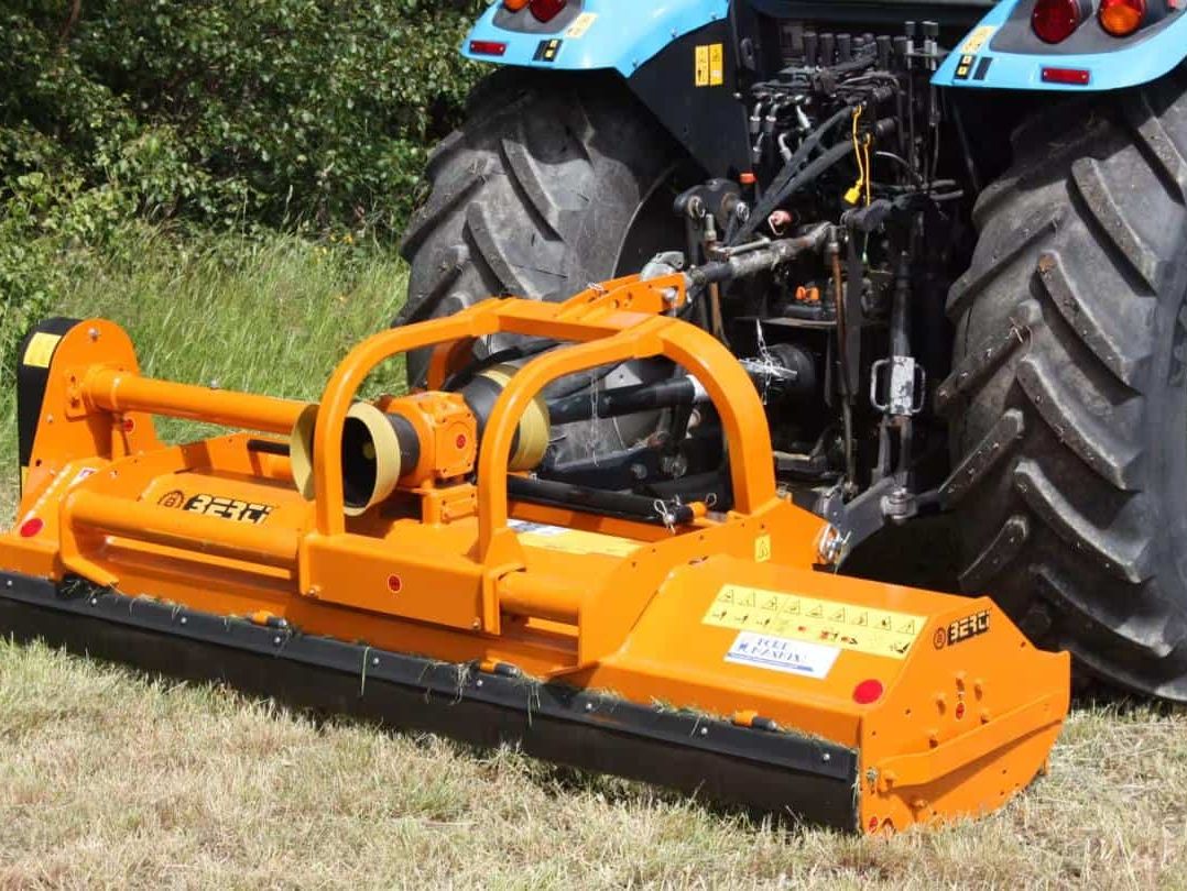 Oransje beitepusser montert på traktor klargjort for arbeid.