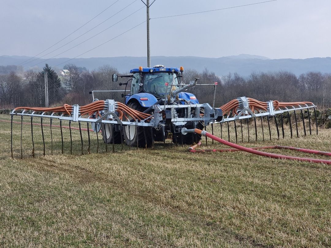 Rød traktor med slåmaskin står på en eng med nyslått gress en solrik dag.