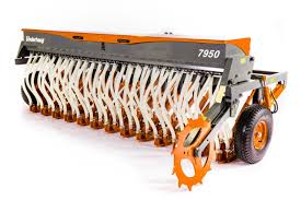 Rød traktor med slåmaskin står på en eng med nyslått gress en solrik dag.