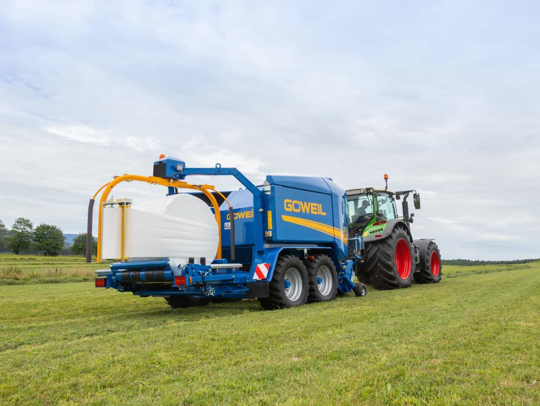 Traktor trekker blå Goweil rundballepresse og pakker på jordet.