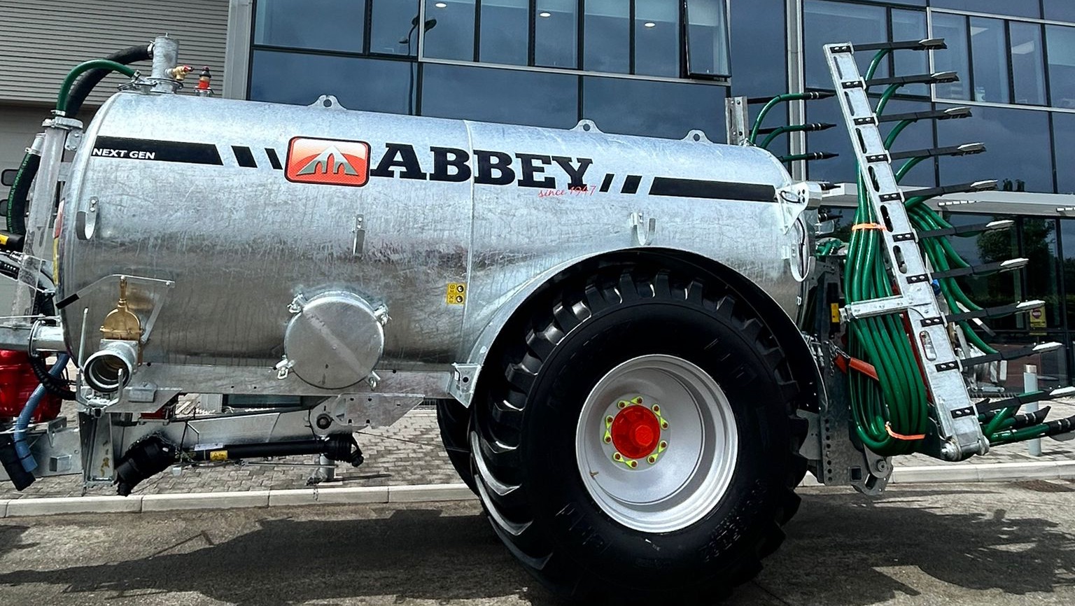 Rød traktor med slåmaskin står på en eng med nyslått gress en solrik dag.