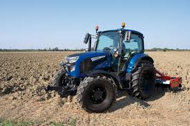 En grønn traktor med rundballepakker som pakker høyballer i plast ute på et jorde.