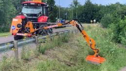 Rød traktor med slåmaskin står på en eng med nyslått gress en solrik dag.