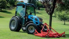 En grønn traktor med rundballepakker som pakker høyballer i plast ute på et jorde.