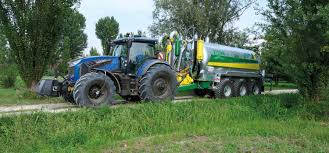 En grønn traktor med rundballepakker som pakker høyballer i plast ute på et jorde.