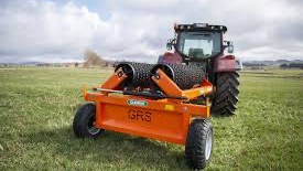 Rød traktor med slåmaskin står på en eng med nyslått gress en solrik dag.