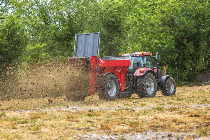 Rød traktor med slåmaskin står på en eng med nyslått gress en solrik dag.
